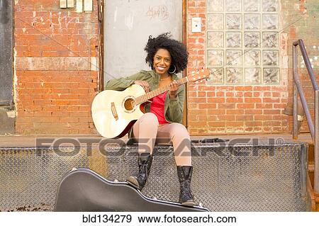 Mixed race woman playing guitar in city View Large Photo Image Stock Photo - Mixed race woman playing guitar in city. Fotosearch