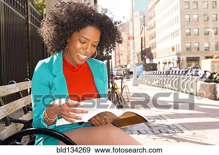 Stock Photo - Mixed race woman reading on city bench. Fotosearch