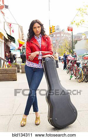Stock Image - Mixed race woman with guitar case on city sidewalk. Fotosearch