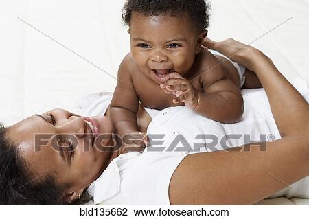 Stock Image - Mother and baby playing on bed. Fotosearch