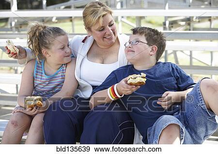 Stock Photo - Mother and children eating sandwiches on bleachers. Fotosearch