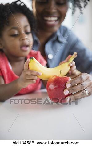 Stock Photograph - Mother and daughter playing with fruit. Fotosearch