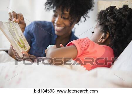 Stock Image - Mother and daughter reading in bed. Fotosearch