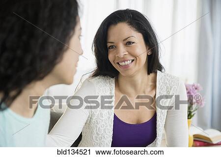Stock Image - Mother and daughter talking in living room. Fotosearch