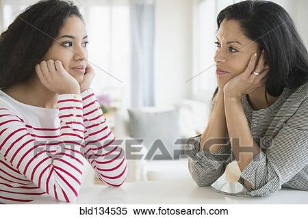 Stock Photography - Mother and daughter with heads in hands at table. Fotosearch