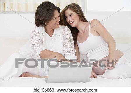 Stock Image - Mother and pregnant daughter using laptop. Fotosearch