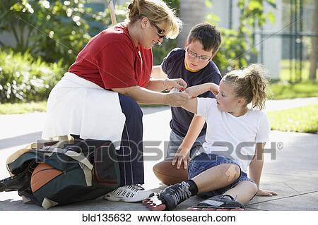 Stock Image - Mother bandaging daughter's scrape. Fotosearch