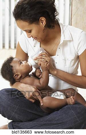Stock Image - Mother bottle feeding baby. Fotosearch