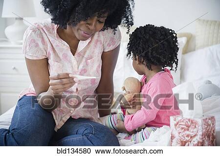 Stock Image - Mother checking daughter's temperature on bed. Fotosearch