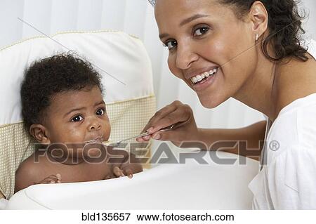 Mother feeding baby in high chair View Large Photo Image Stock Photo - Mother feeding baby in high chair. Fotosearch