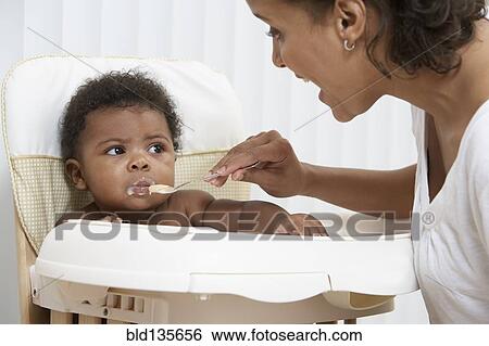 Mother feeding baby in high chair View Large Photo Image Stock Photograph - Mother feeding baby in high chair. Fotosearch