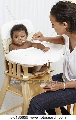 Stock Photography - Mother feeding baby in high chair. Fotosearch