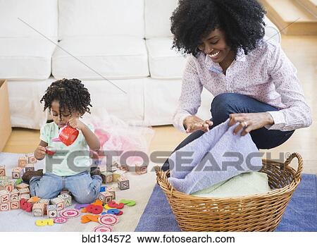Mother folding laundry while daughter plays View Large Photo Image Stock Image - Mother folding laundry while daughter plays. Fotosearch