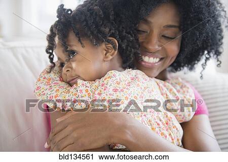 Stock Image - Mother hugging daughter on sofa. Fotosearch