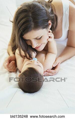 Stock Photo - Mother playing with baby on bed. Fotosearch