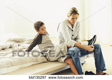 Mother putting son's shoes on on bed View Large Photo Image Stock Photo - Mother putting son's shoes on on bed. Fotosearch