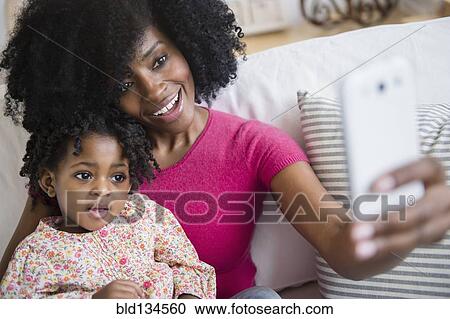 Mother taking photograph with daughter on sofa View Large Photo Image Stock Image - Mother taking photograph with daughter on sofa. Fotosearch