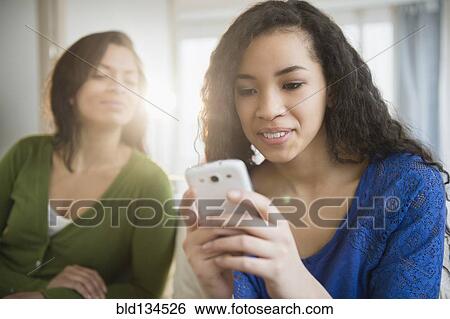 Stock Photograph - Mother watching daughter use cell phone. Fotosearch