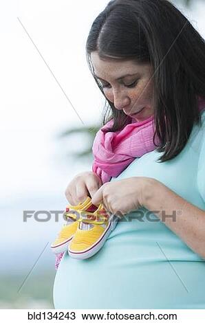 Stock Image - Pregnant Hispanic woman holding baby shoes. Fotosearch