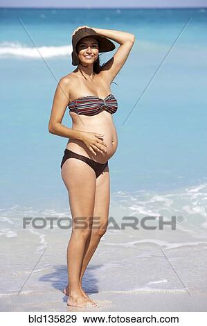 Stock Photo - Pregnant Hispanic woman standing on beach. Fotosearch