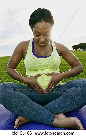 Stock Photograph - Pregnant woman holding her stomach in park. Fotosearch