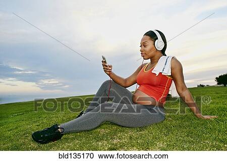 Pregnant woman listening to headphones in park View Large Photo Image Stock Image - Pregnant woman listening to headphones in park. Fotosearch