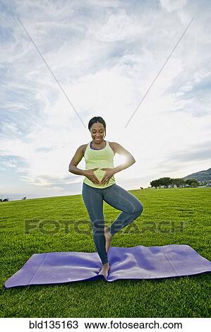 Stock Image - Pregnant woman practicing yoga in park. Fotosearch