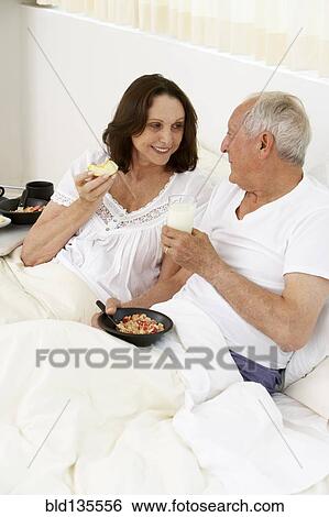 Senior couple eating breakfast in bed View Large Photo Image Stock Photograph - Senior couple eating breakfast in bed. Fotosearch