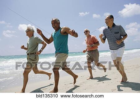 Stock Image - Senior couples jogging on beach. Fotosearch