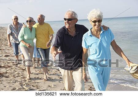 Stock Image - Senior couples walking on beach. Fotosearch