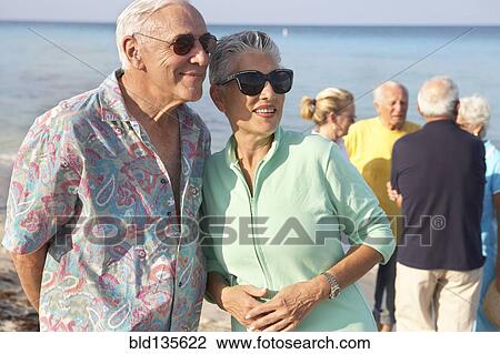 Stock Image - Senior couples walking on beach. Fotosearch