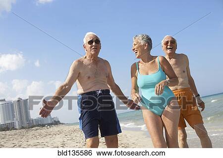 Stock Photograph - Senior friends relaxing on beach. Fotosearch