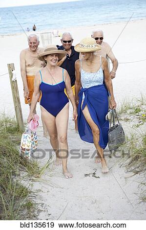 Stock Photo - Senior friends walking on beach. Fotosearch
