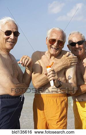 Senior men applying sunscreen on beach View Large Photo Image Stock Photograph - Senior men applying sunscreen on beach. Fotosearch