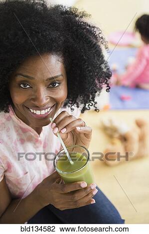 Stock Image - Smiling woman drinking green juice. Fotosearch