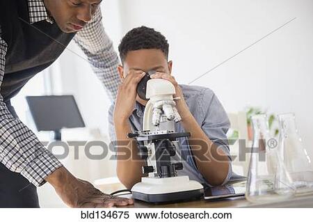 Stock Photography - Teacher helping student use microscope in science class. Fotosearch