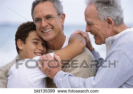 Stock Photo - Three generations of Caucasian men hugging on beach. Fotosearch