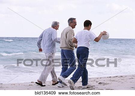 Stock Photo - Three generations of Caucasian men walking on beach. Fotosearch