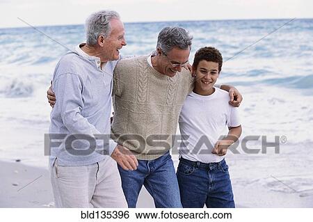 Stock Photograph - Three generations of Caucasian men walking on beach. Fotosearch