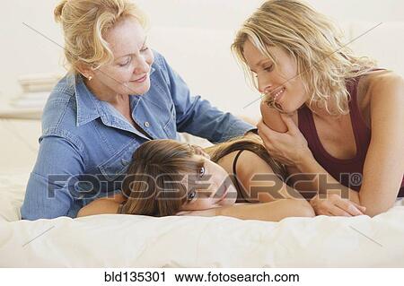 Stock Image - Three generations of women laying on bed. Fotosearch
