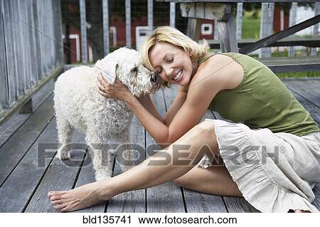Stock Image - Woman petting dog on wooden patio. Fotosearch
