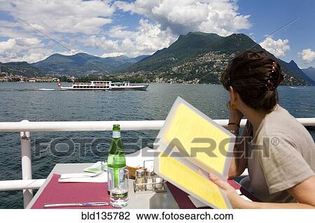 Woman reading menu in restaurant overlooking rural lake, Lugano, Ticino, Switzerland View Large Photo Image Stock Image - Woman reading menu in restaurant overlooking rural lake, Lugano, Ticino, Switzerland. Fotosearch