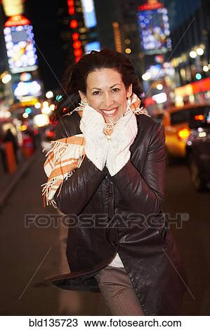 Stock Image - Woman smiling on city street lit up at night, New York City, New York, United States, . Fotosearch