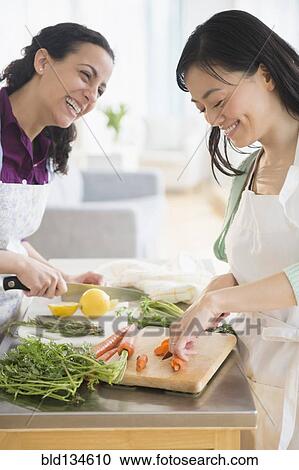 Stock Image - Women chopping vegetables together. Fotosearch