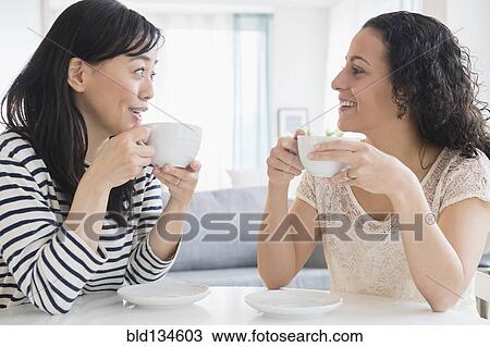 Stock Image - Women drinking coffee together at table. Fotosearch