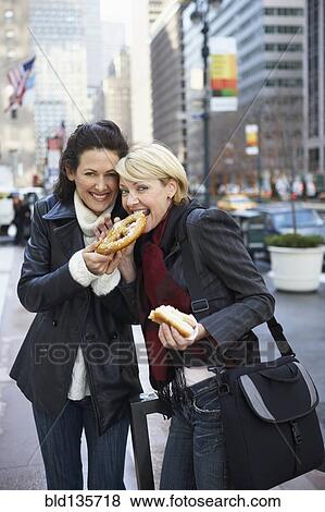 Women eating pretzel on city street View Large Photo Image Stock Photo - Women eating pretzel on city street. Fotosearch
