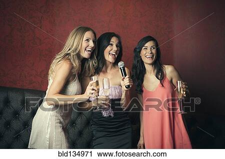 Stock Image - Women singing karaoke together in nightclub. Fotosearch