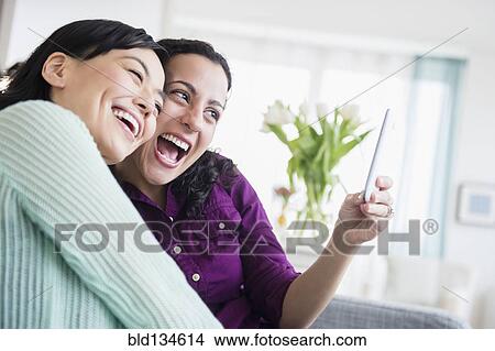Picture - Women taking picture together in living room. Fotosearch