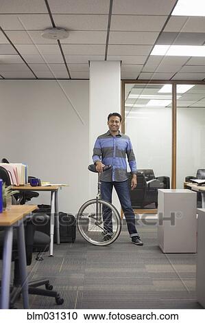 Stock Image - Asian businessman holding unicycle in office. Fotosearch
