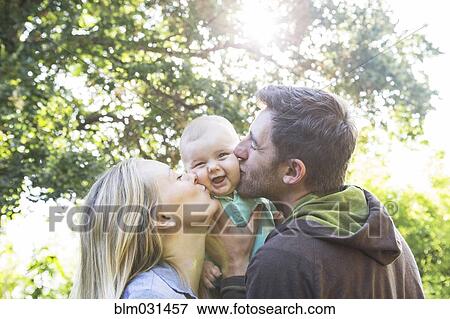 Stock Photo - Caucasian couple kissing baby in backyard. Fotosearch